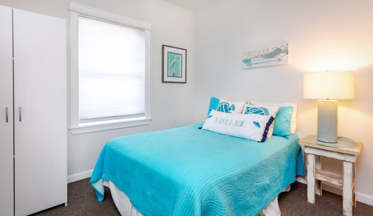 A small bedroom with a blue bed and white dresser.