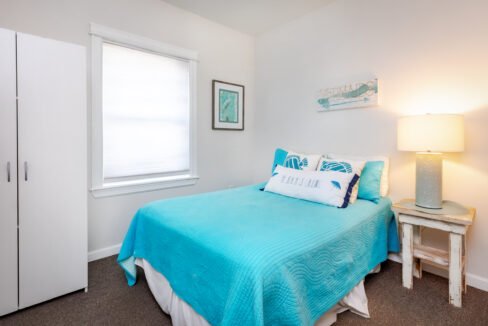 A small bedroom with a blue bed and white dresser.