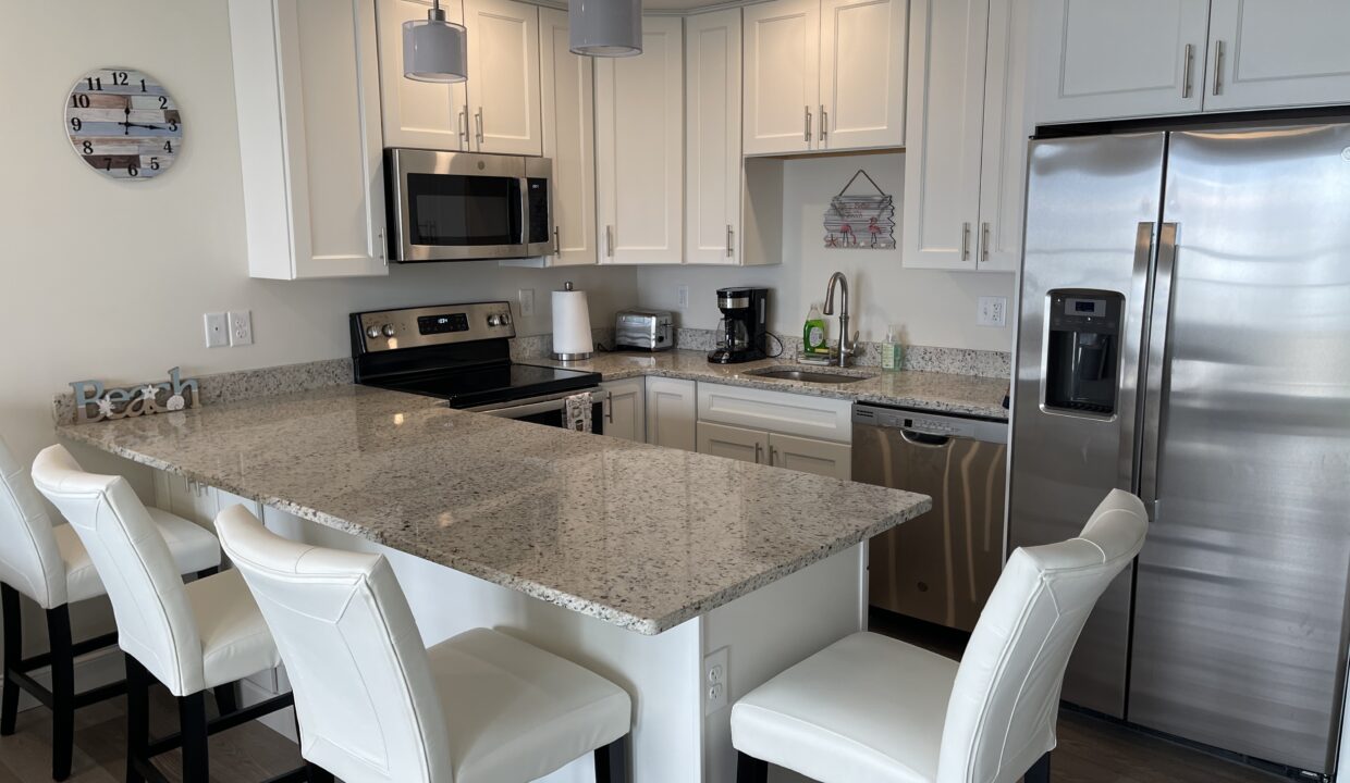 a kitchen with a refrigerator, stove, sink, and chairs.