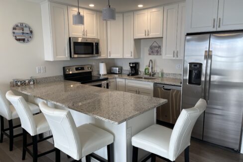 a kitchen with a refrigerator, stove, sink, and chairs.