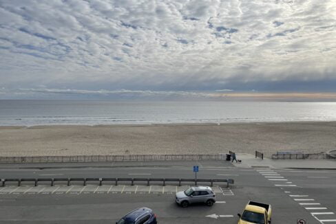 a parking lot next to a beach with cars parked in it.