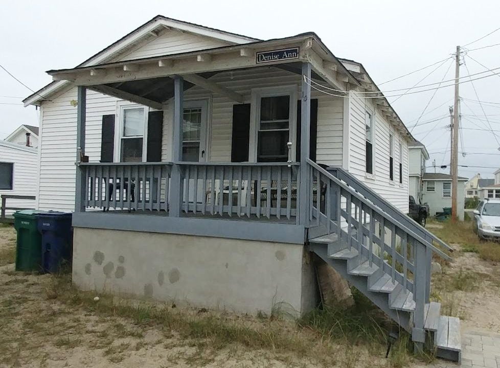 a small white house with a porch and stairs.