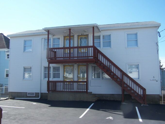 a two story white building with a red stair case.