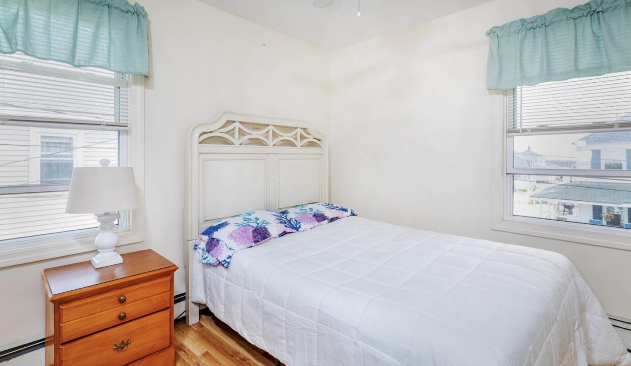 a bedroom with a bed, dresser, and two windows.