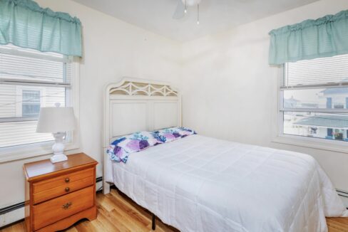 a bedroom with a bed, dresser, and two windows.