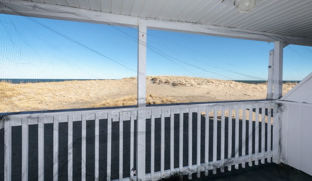 Porch with a white railing overlooking a sandy landscape under a clear blue sky.