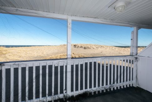 Porch with a white railing overlooking a sandy landscape under a clear blue sky.