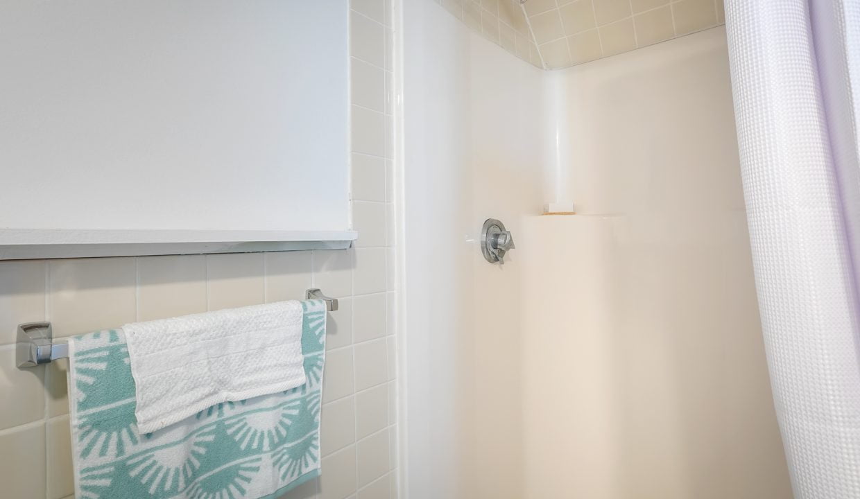 A well-lit, clean bathroom with a shower, white tiled walls, and a patterned towel hanging on a rack.
