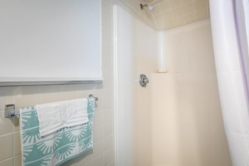 A well-lit, clean bathroom with a shower, white tiled walls, and a patterned towel hanging on a rack.