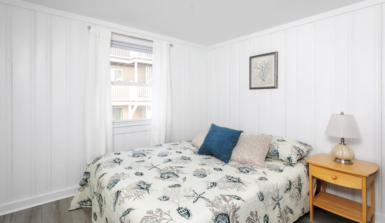 A bright, neatly organized bedroom with botanical-themed bedding, a wooden nightstand, and a table lamp.