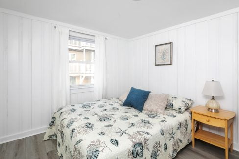 A bright, neatly organized bedroom with botanical-themed bedding, a wooden nightstand, and a table lamp.