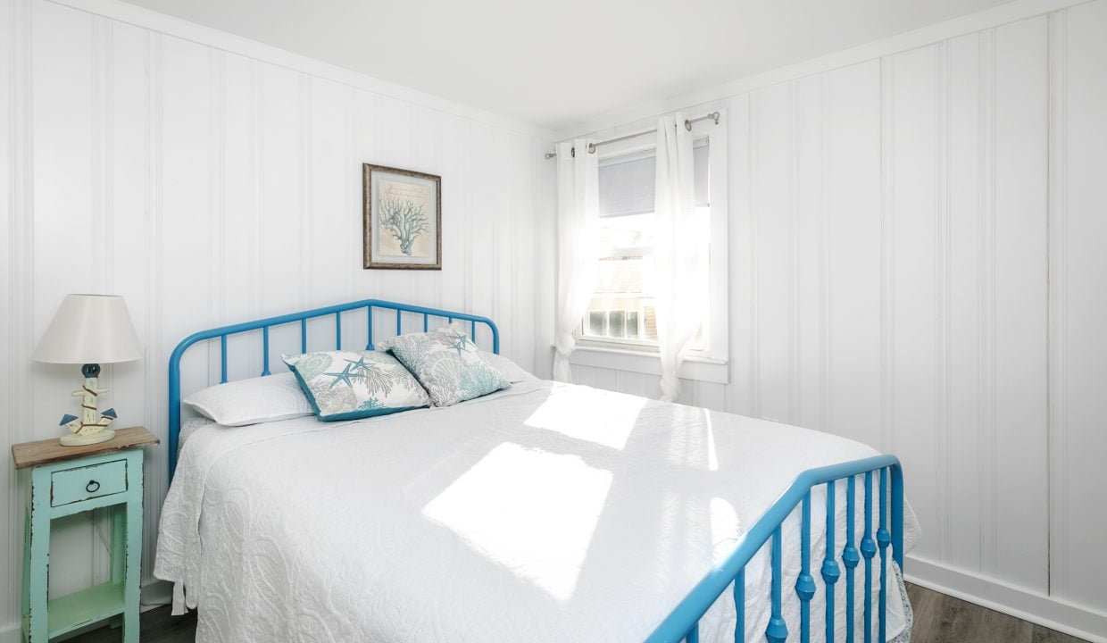 Bright and airy bedroom with a blue bed frame and white linens, accented by blue patterned pillows and a picture on the wall.