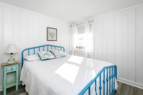 Bright and airy bedroom with a blue bed frame and white linens, accented by blue patterned pillows and a picture on the wall.