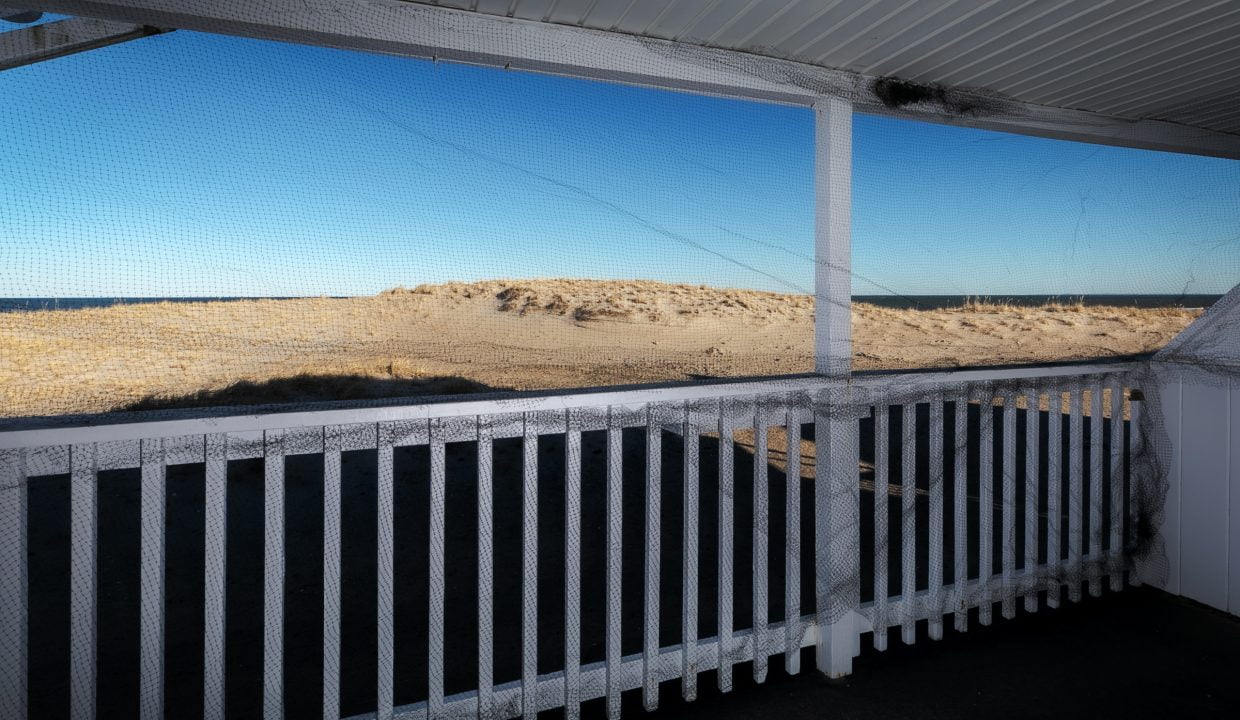 A screened porch with a view of sand dunes under a clear sky.
