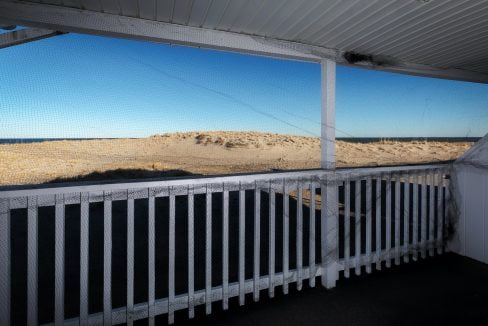 A screened porch with a view of sand dunes under a clear sky.