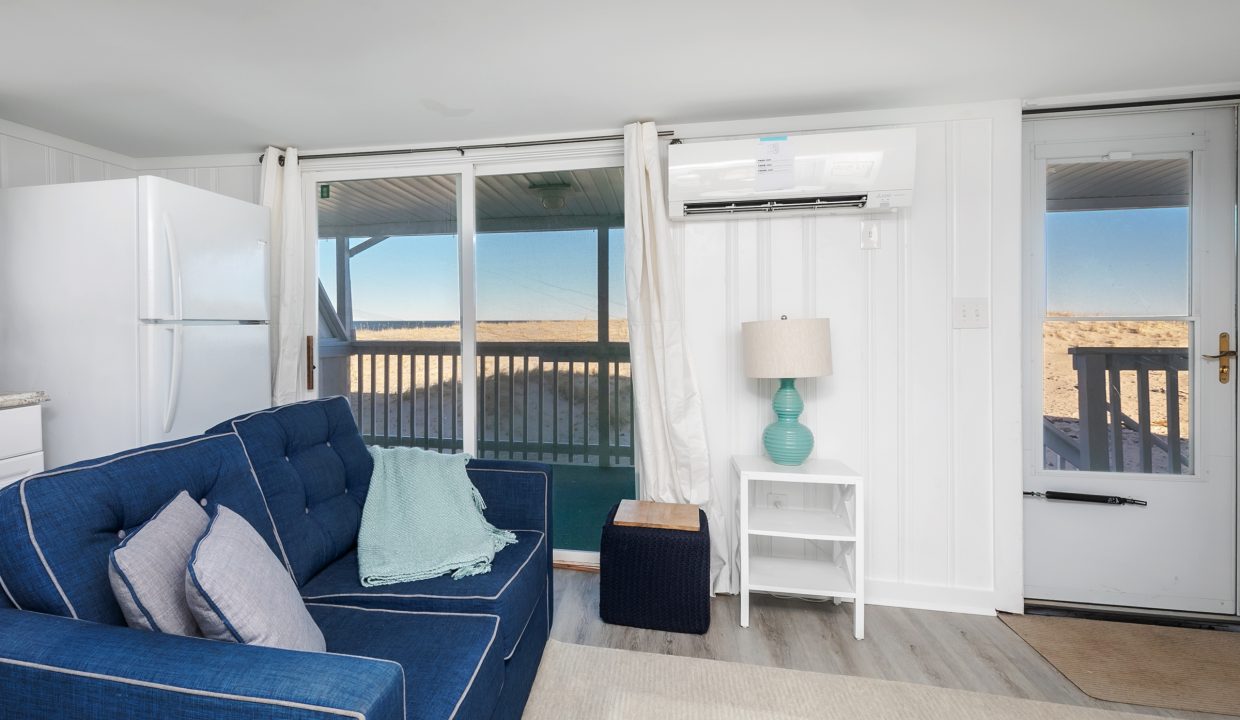Beachfront apartment interior with a blue sofa, white furnishings, and a balcony overlooking the sea.