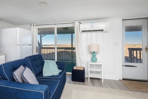 Beachfront apartment interior with a blue sofa, white furnishings, and a balcony overlooking the sea.