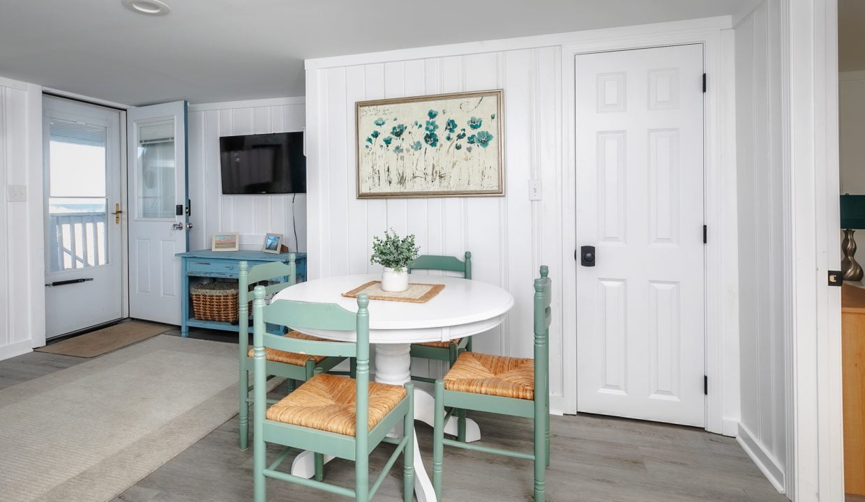 Bright coastal-themed dining area with a white round table, green chairs, and a floral wall art piece.