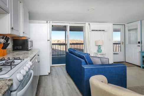 Cozy beachfront apartment interior with an open-plan kitchen and living room leading to a balcony with a view of the dunes.