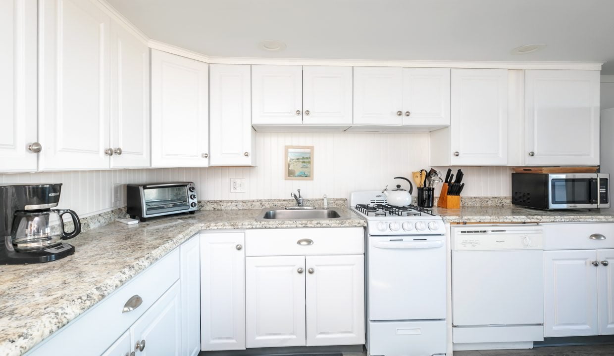 A bright, modern kitchen with white cabinetry and granite countertops equipped with various appliances.