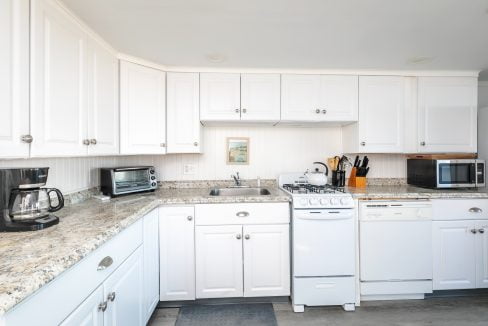 A bright, modern kitchen with white cabinetry and granite countertops equipped with various appliances.