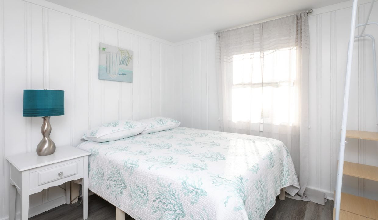 Bright and airy bedroom with white walls, a bed with teal bedding, and a matching bedside lamp.