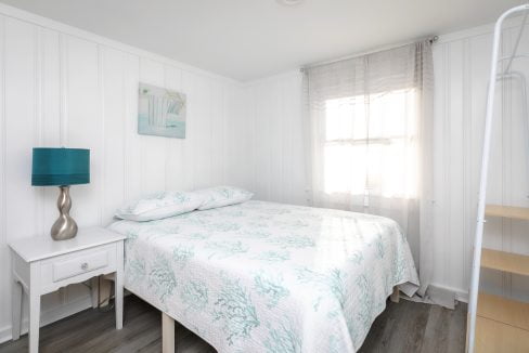 Bright and airy bedroom with white walls, a bed with teal bedding, and a matching bedside lamp.