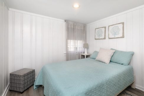 A bright, minimalistic bedroom with a neatly made bed, light-colored walls, and simple decor.