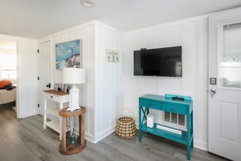 A bright, coastal-themed room with white paneling, a mounted tv, and turquoise accents.