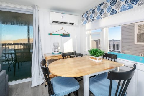 Bright coastal-themed dining area with a wooden table, blue chairs, and sliding door leading to a balcony.