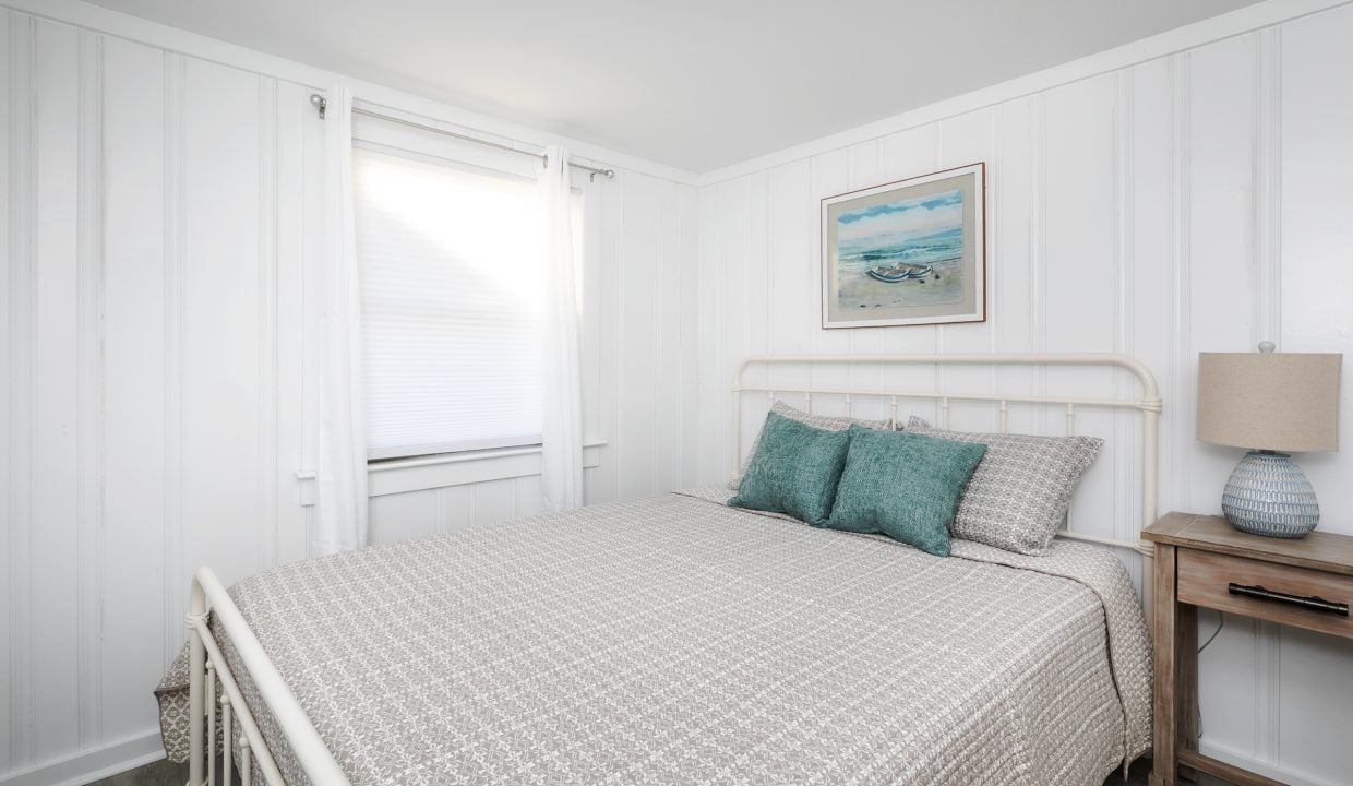 Bright, cozy bedroom with a white interior, double bed, and beach-themed decor.