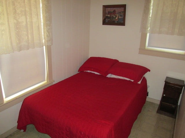 a bed with a red comforter and two windows.