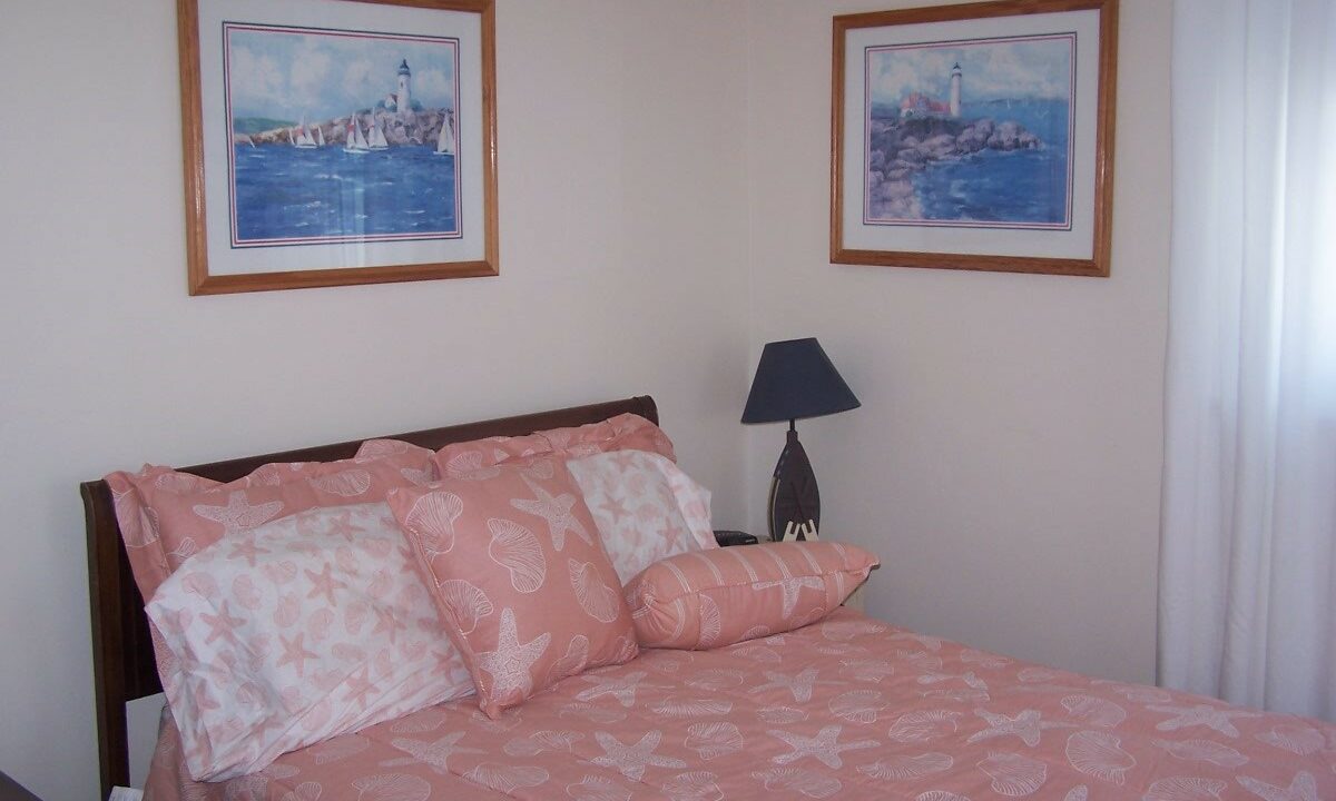 a bed with a pink comforter and two pictures on the wall.