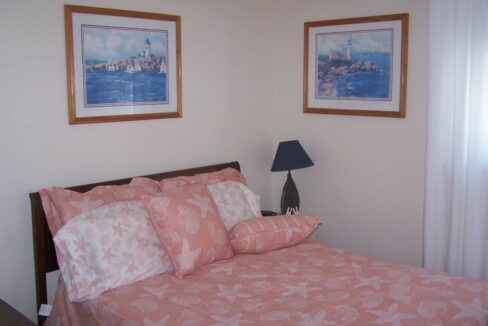 a bed with a pink comforter and two pictures on the wall.