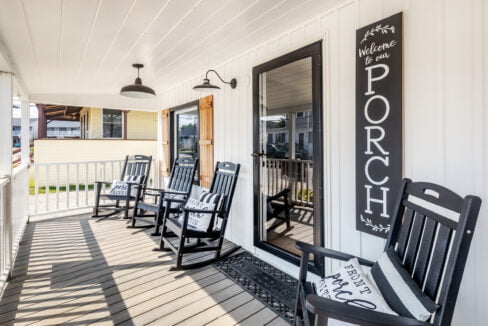 A porch with rocking chairs and a sign.
