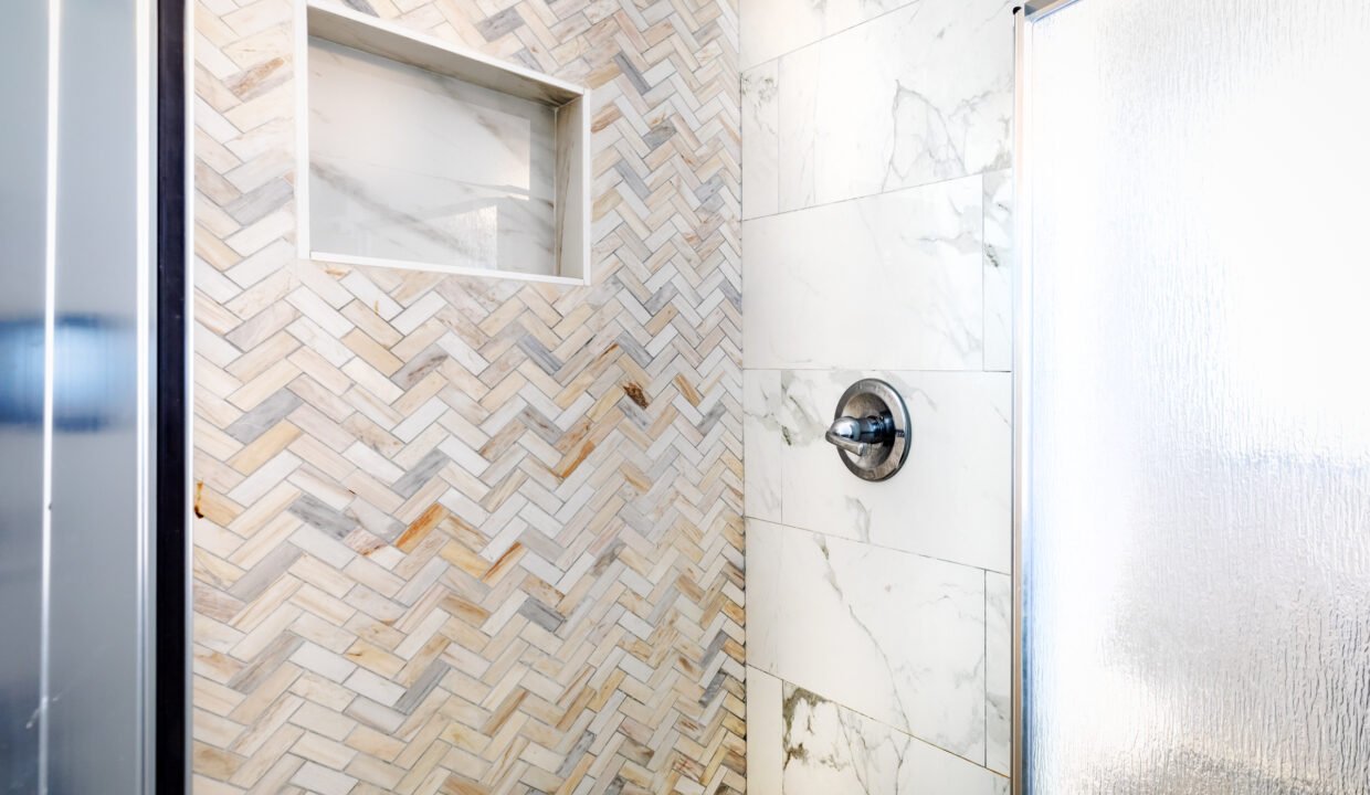 A herringbone tiled shower with a glass door.