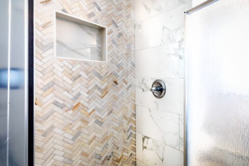 A herringbone tiled shower with a glass door.