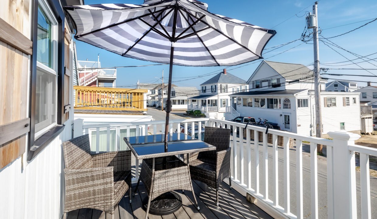 A wicker table and umbrella on a deck with a view of the ocean.