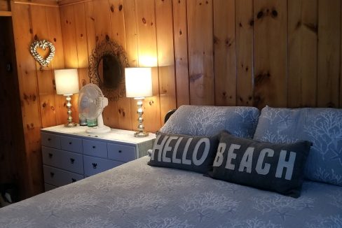 A bed in a bedroom with wood paneling and a hello beach sign.