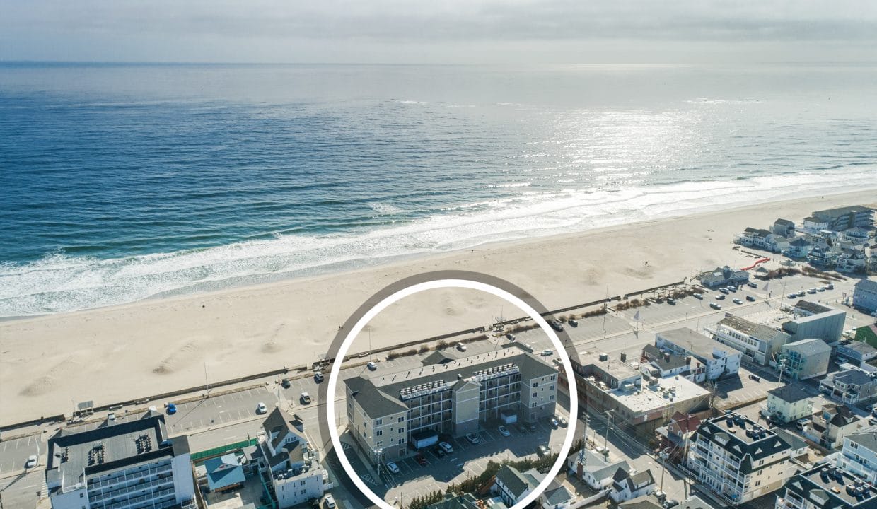Aerial view of a beachfront neighborhood with a circular highlight around a specific building facing the ocean and sandy beach.