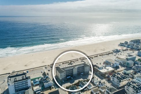 Aerial view of a beachfront neighborhood with a circular highlight around a specific building facing the ocean and sandy beach.