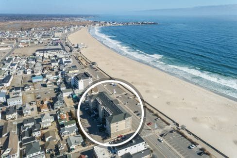 Aerial view of a coastal town with a sandy beach and ocean waves; a building near the shoreline is highlighted with a white circle.