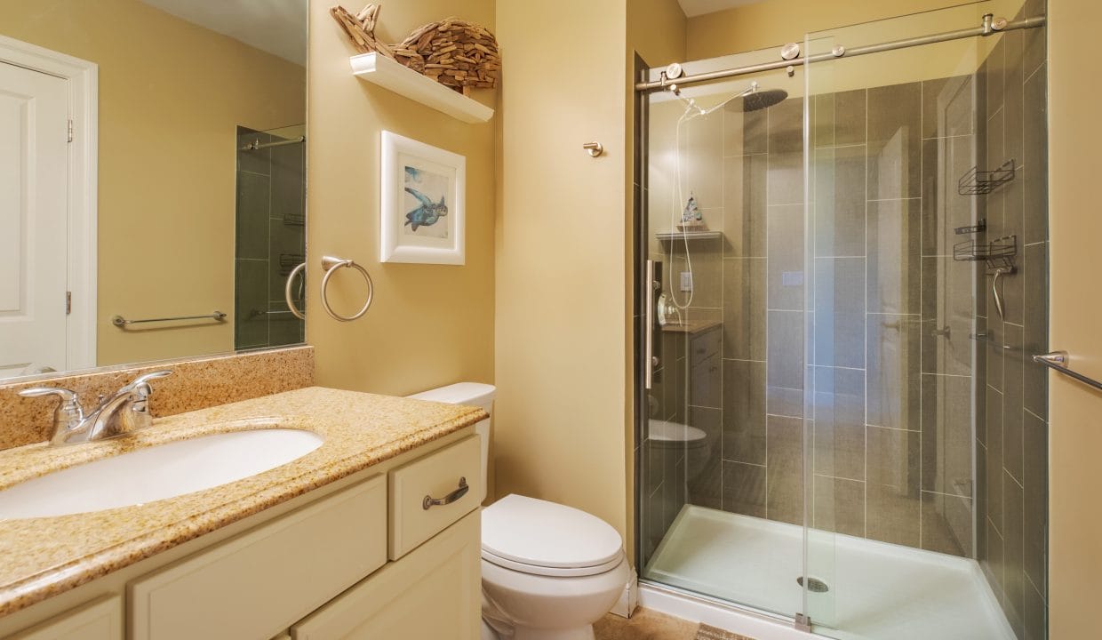 Bathroom with beige walls, granite countertop, white vanity, toilet, glass-enclosed shower, and wall art above the towel ring.