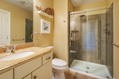 Bathroom with beige walls, granite countertop, white vanity, toilet, glass-enclosed shower, and wall art above the towel ring.