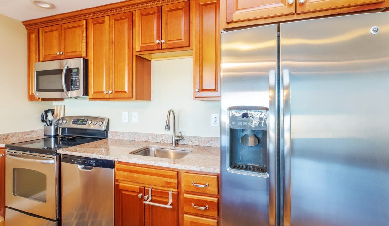 Modern kitchen with stainless steel appliances, including a refrigerator, microwave, oven, and dishwasher, wooden cabinets, and a sink with a faucet under a cabinet.