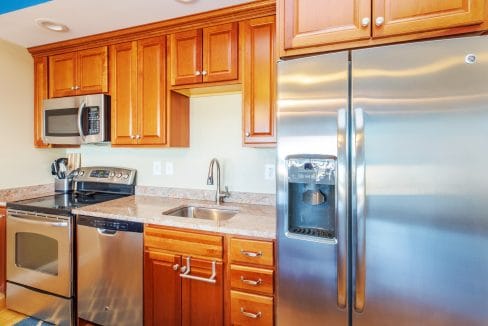 Modern kitchen with stainless steel appliances, including a refrigerator, microwave, oven, and dishwasher, wooden cabinets, and a sink with a faucet under a cabinet.