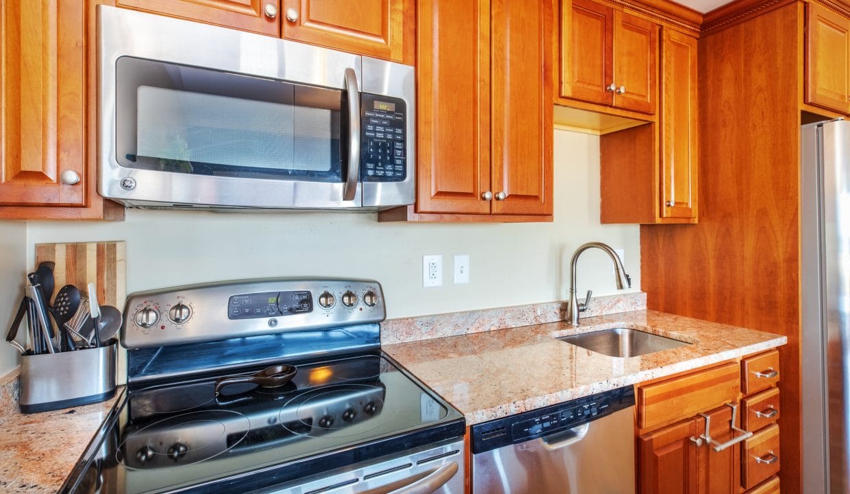Modern kitchen with wooden cabinets, stainless steel appliances, electric stove, built-in microwave, dishwasher, sink, and a knife block on a granite countertop.
