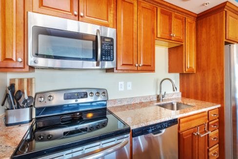 Modern kitchen with wooden cabinets, stainless steel appliances, electric stove, built-in microwave, dishwasher, sink, and a knife block on a granite countertop.