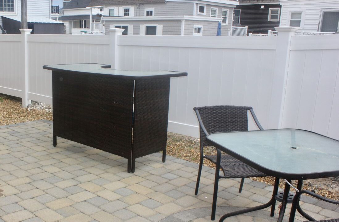 a patio with a table and chairs next to a white fence.