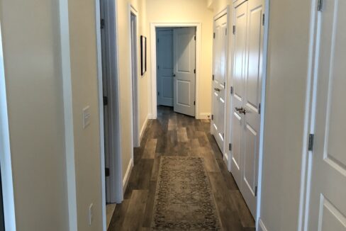a long hallway with wooden floors and white doors.